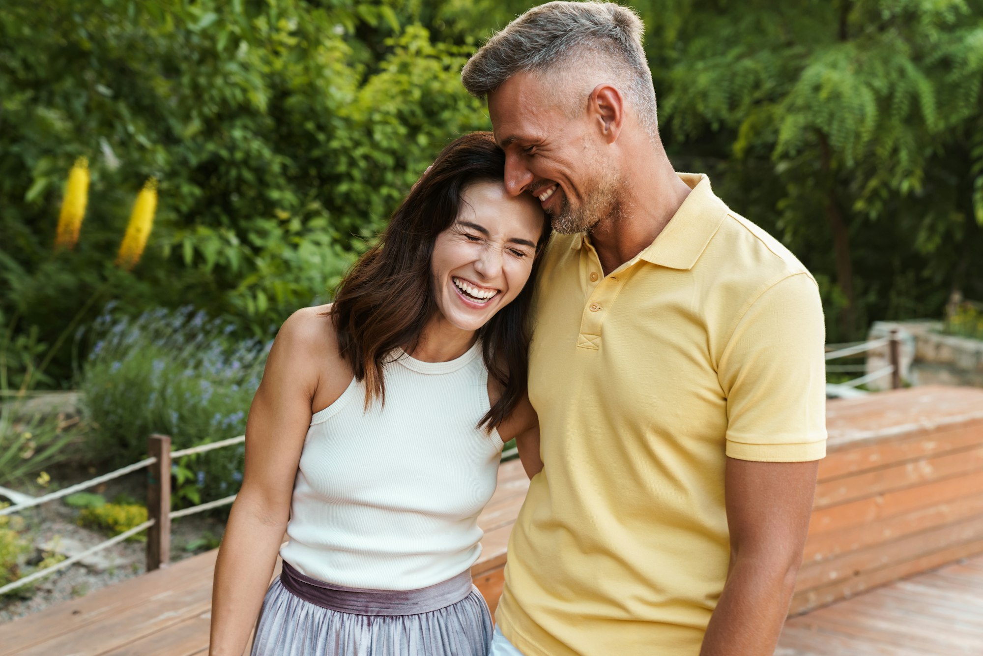 Portrait of joyful middle-aged couple aughing and hugging while walking in summer park