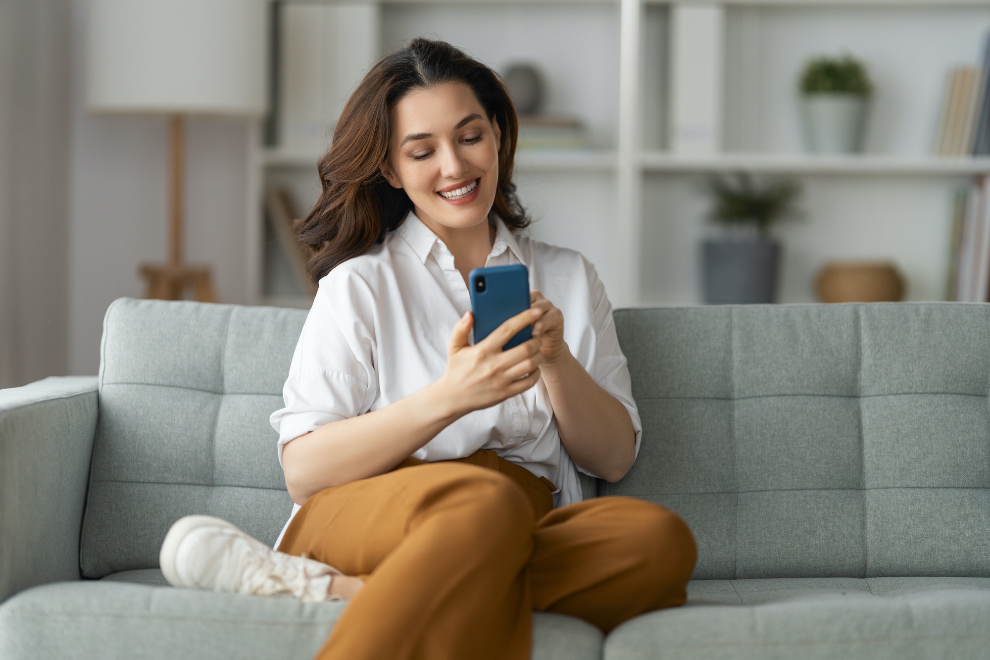 woman is using a phone sitting on a sofa