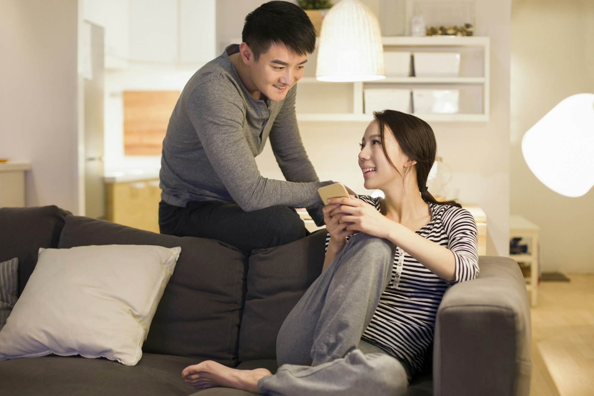 Young couple using smart phone on living room sofa