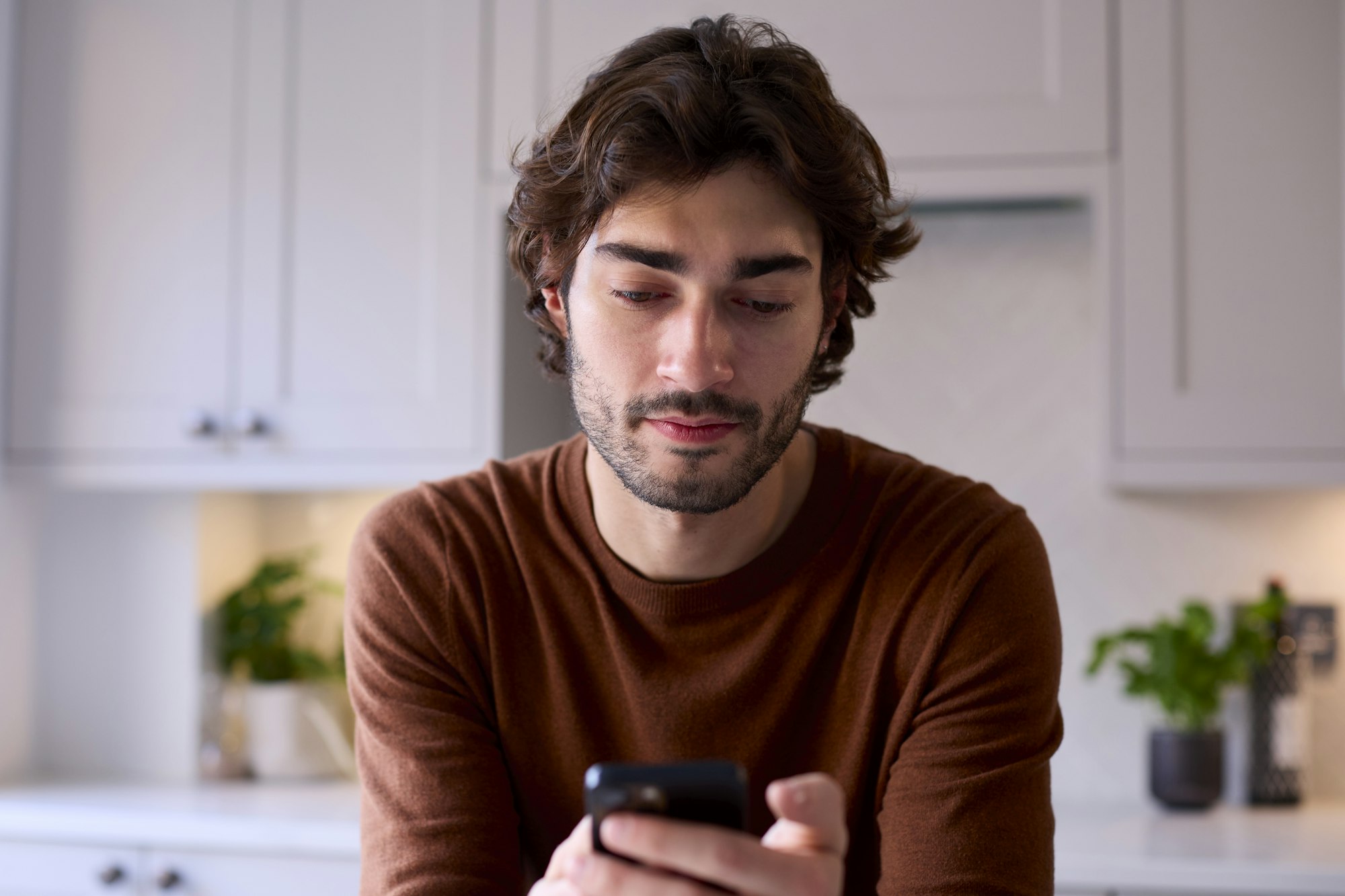 Young Man Relaxing At Home In Kitchen Checking Messages Social Media On Mobile Phone