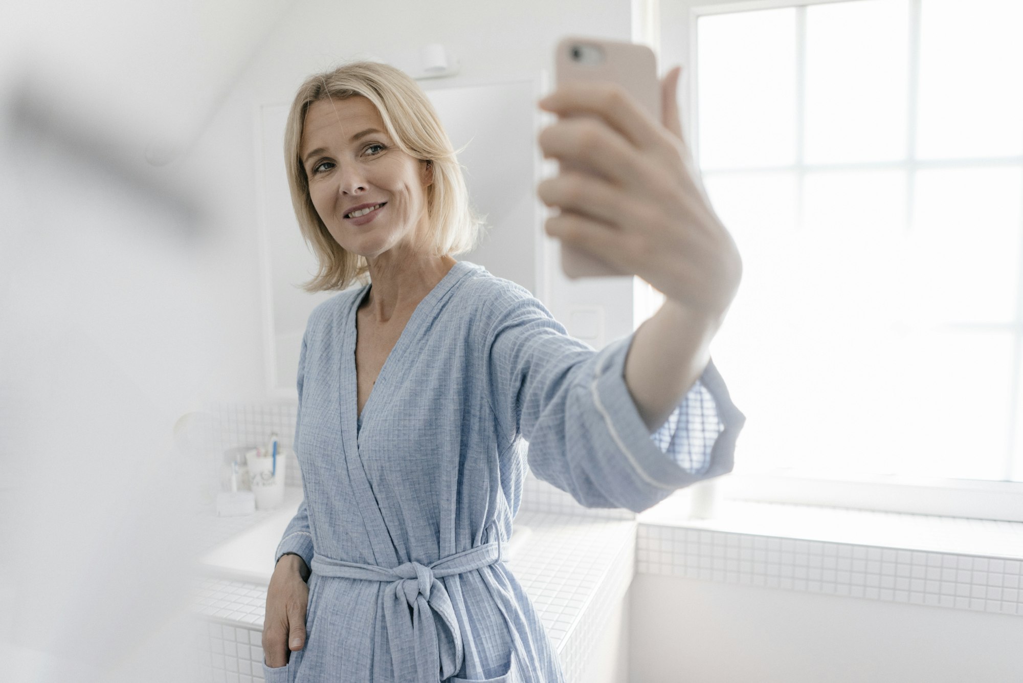 Smiling mature woman taking a selfie in bathroom