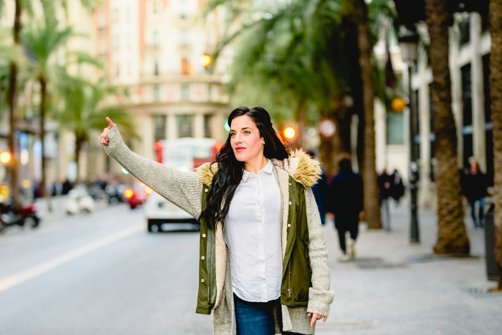 Middle-aged woman hailing a taxi with her hand raised in the street.