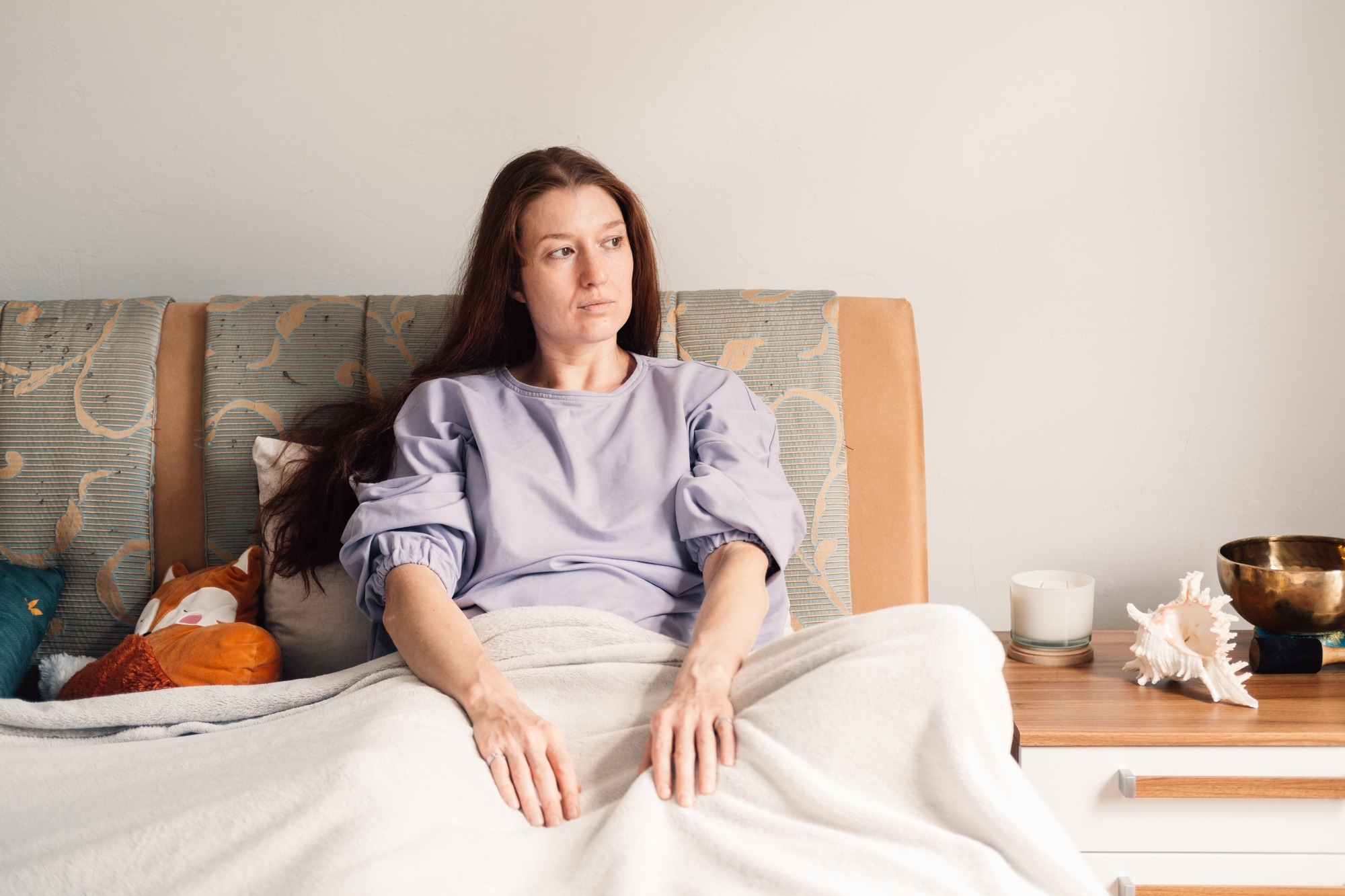 A thoughtful woman sits in quiet contemplation on her couch, embodying a moment of solitude
