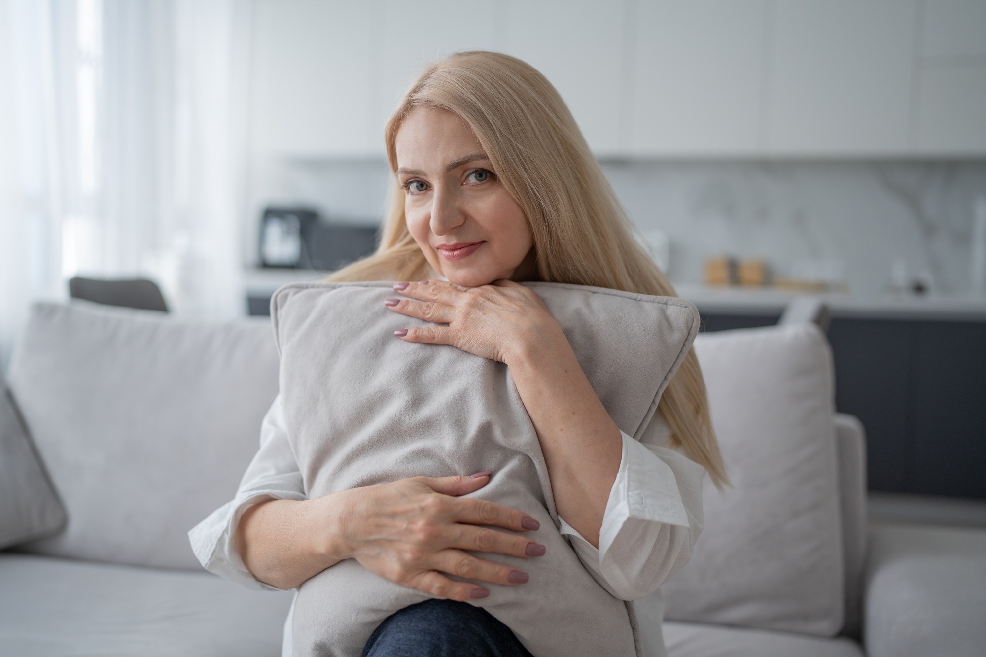 Woman on a couch in a modern living room, hugging a pillow in peaceful solitude